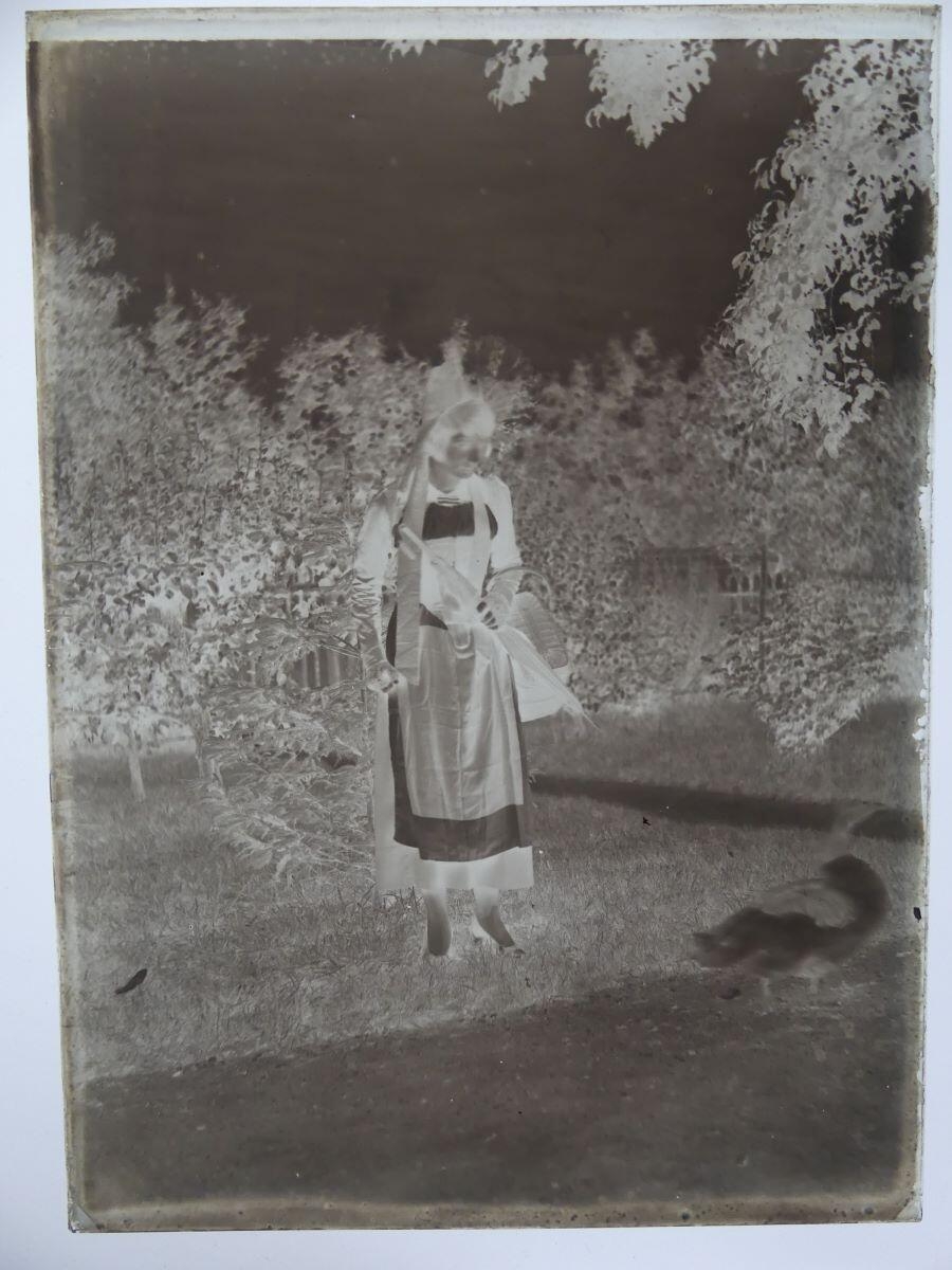 Jeune femme en costume régional, tenant un parapluie fermé, dans un jardin_1