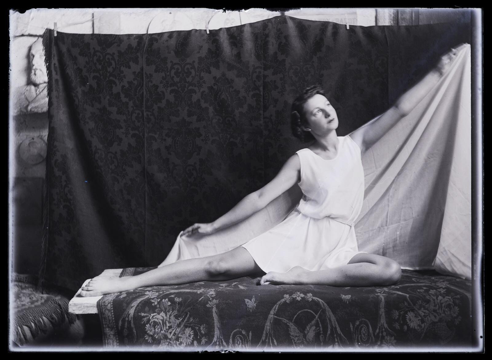 Modèle féminin posant dans l'atelier, assise, les bras ouverts et tenant un voile derrière elle_0