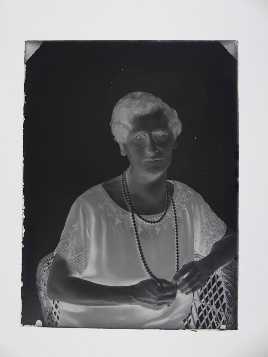 Portrait d'une femme portant des lunettes et un sautoir en perles, assise dans un fauteuil en osier, Louis Hertig, 1ère moitié 20e siècle