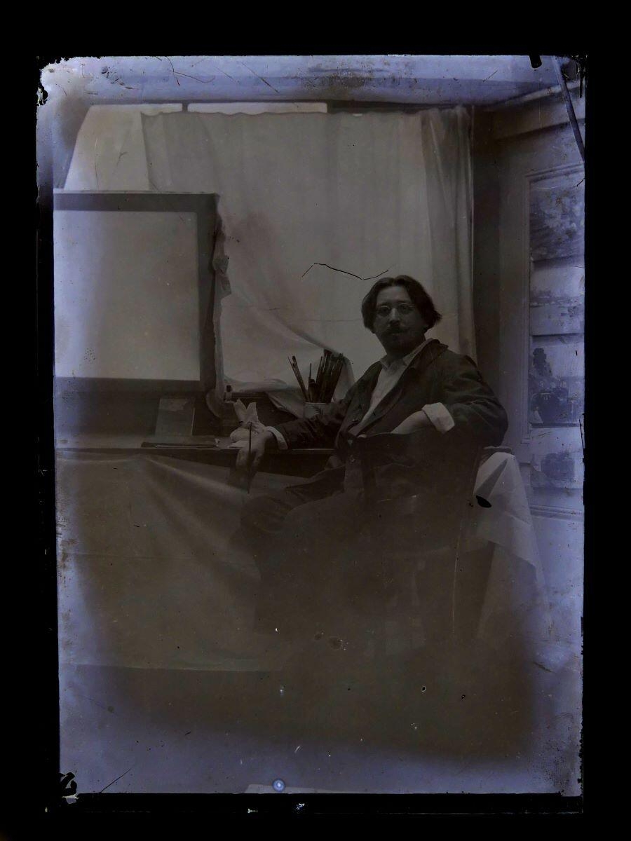 Portrait du peintre Léon Tirode dans son atelier assis devant une table de travail, assis sur la droite, Studio Meusy, 4e quart 19e siècle, 1ère moitié 20e siècle