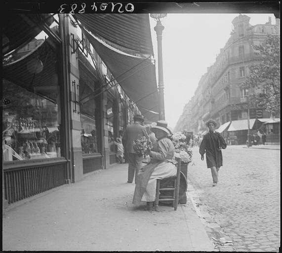 Scène animée : passants sur le trottoir, devantures de boutiques