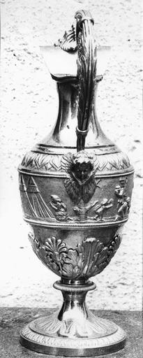 burette de Monseigneur Pons sur le thème de l'eau, argent, 19e siècle, vue du revers, avec extrémité inférieure de la anse ornée d'une tête d'ange, et sur la panse la scène des hébreux trouvant de l'eau dans le désert suite au frappement du rocher par Moïse - © Ministère de la Culture (France), Médiathèque du patrimoine et de la photographie (objets mobiliers), tous droits réservés