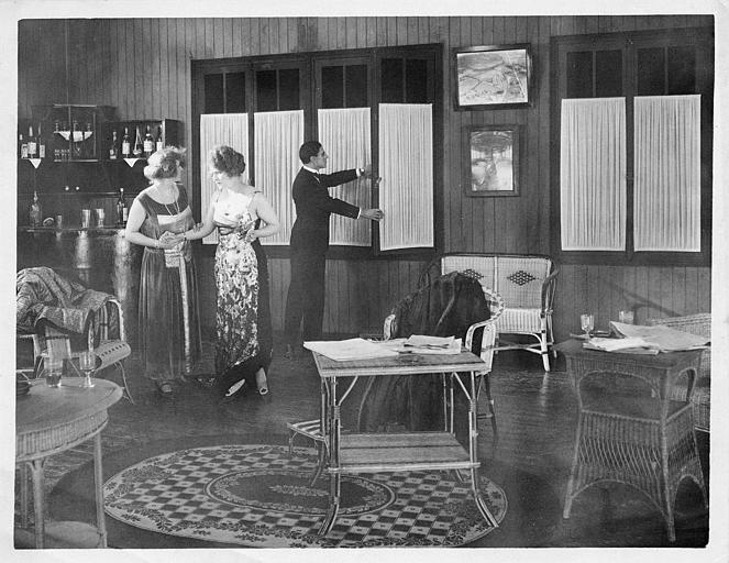 Dans un salon, deux femmes et un homme fermant la fenêtre