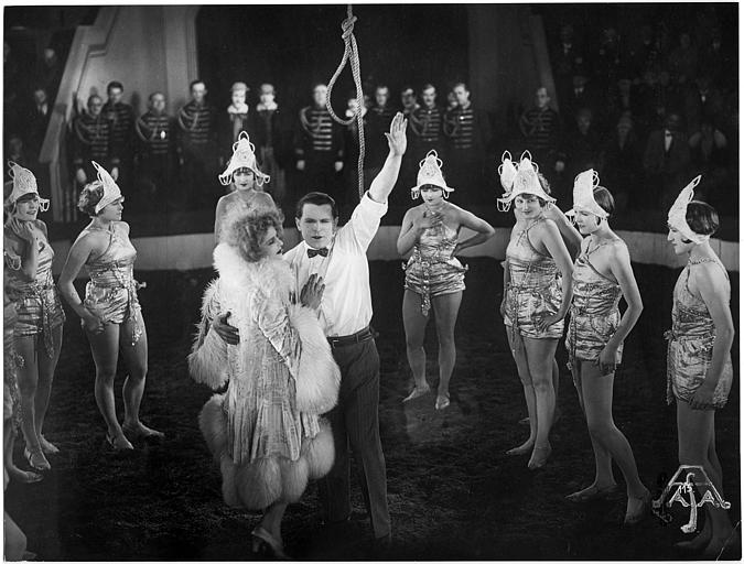 Luciano Albertini jouant Silvio Spaventa au milieu d'une piste de cirque, entouré de plusieurs femmes