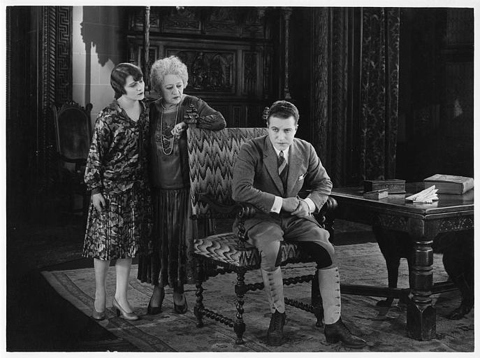 Aimé Simon-Girard, dans le rôle de Jacques de la Ferlandière, assis sur une chaise avec deux femmes dans son dos