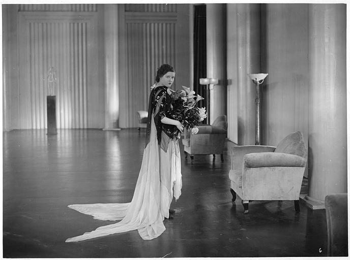 Marie Glory portant un bouquet de lys dans une grande pièce