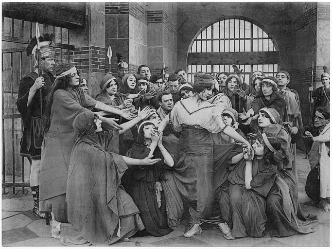 Dans une prison à l'époque antique, une femme entourée de plusieurs personnages dont la majorité sont des femmes