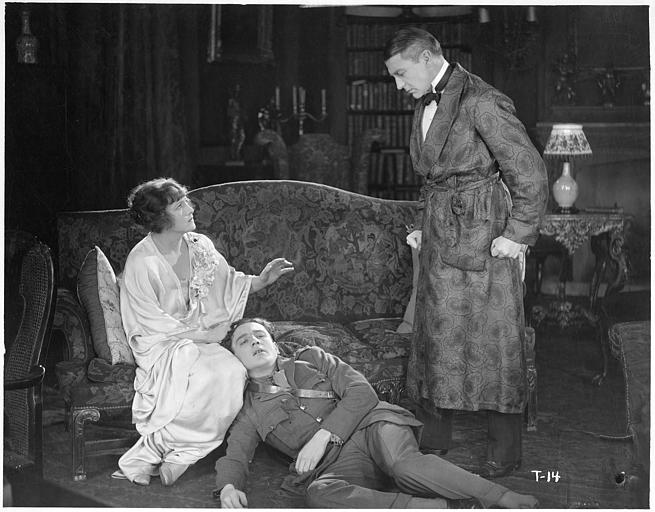 Un homme au sol dans un salon entouré de Fay Compton dans le rôle de Rosalie Aubyn et d'un homme en robes de chambre