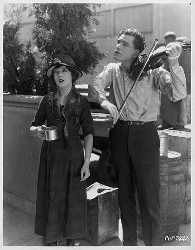 Dans la rue, May McAvoy chante pour gagner de l'argent, tandis que Bert Lytell l'accompagne au violon