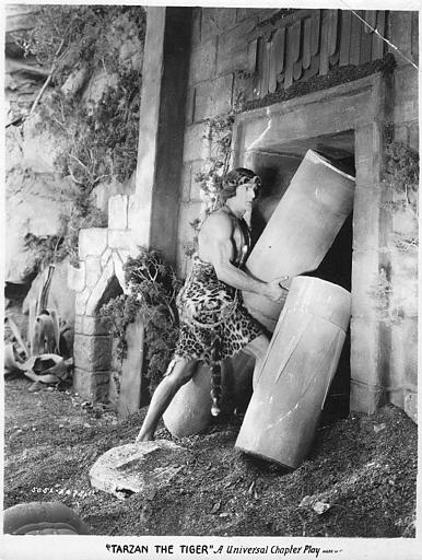 Franck Merril dans le rôle de Tarzan soulevant des morceaux de colonnes à l'entrée d'un temple