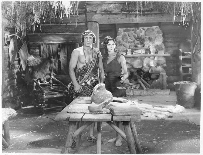 Natalie Kingston dans le rôle Mary Trevor et Franck Merril dans celui de Tarzan devant une table en bois