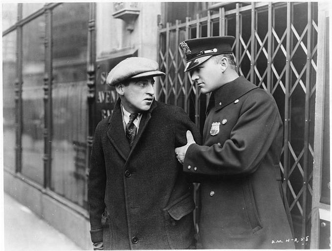 William Boyd dans le rôle de Pete Smith en policier tient le bras d'un homme portant une casquette