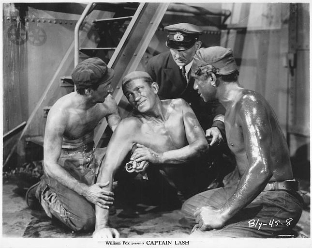 Victor McLaglen est le Capitaine Lash, entouré de trois hommes, au sol dans la cale d'un bateau, au pied d'un escalier métallique