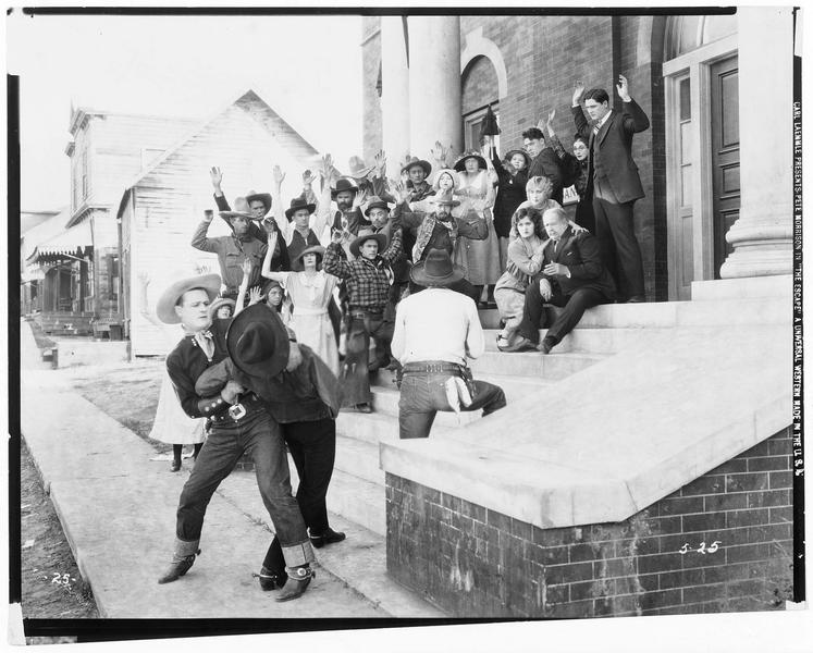 Johnny Bowers (P. Morrison) neutralisant un homme, tandis que son compagnon tient en joue un groupe d'hommes et de femmes à la sortie du temple