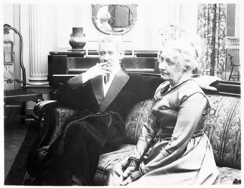 Mrs Carey (G. Claire) assise sur un canapé à côté d'un homme (F. Keenan)