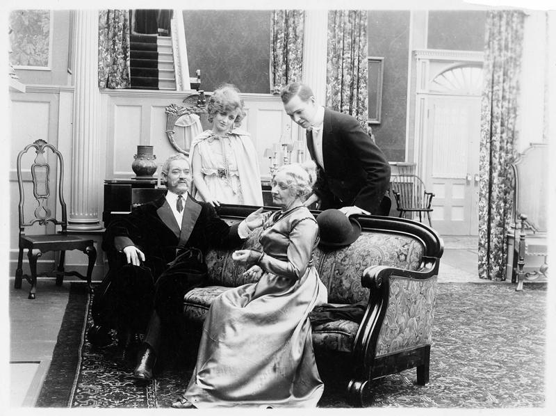 Mrs Carey (G. Claire) assise sur un canapé à côté d'un homme (F. Keenan)