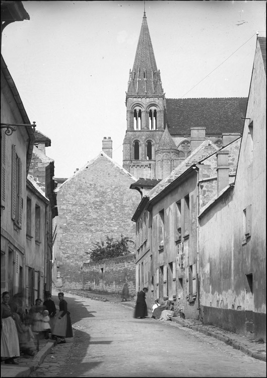 Eglise abbatiale : tour et toitures côté sud, en arrière-plan d’une rue