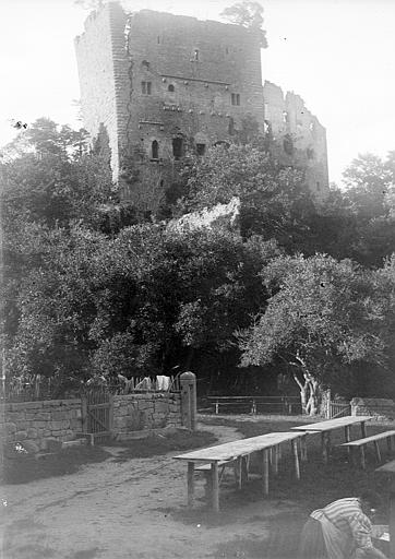 Vue du donjon depuis un jardin où une femme installe les tables pour un repas