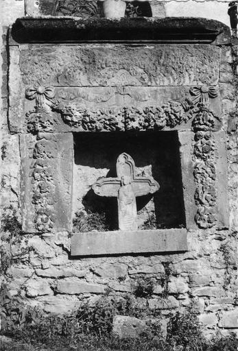 Croix de chemin sculptée en demi-relief de la Vierge à l'Enfant, insérée dans sa niche décorée de guirlandes de fleurs, pierre sculptée