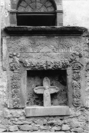 Croix de chemin sculptée en demi-relief de la Vierge à l'Enfant, insérée dans sa niche décorée de guirlandes de fleurs, pierre sculptée