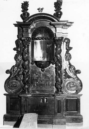 Table de confrérie des Agonisants ornée au centre d'une cuve surmontée d'un conque, flanquée de deux colonnes torses à chapiteaux corinthiens et décorées de rinceaux de vigne grimpante, elles-mêmes flanquées de deux volutes aux chutes de feuilles, au sommet d'un arc en plein cintre se trouvent deux pots à feu, bois sculpté - © Ministère de la Culture (France), Médiathèque du patrimoine et de la photographie (objets mobiliers), tous droits réservés