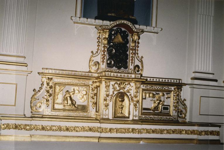 Tabernacle à ailes, sur prédelle en bois doré et polychrome, prédelle ornée d'une guirlande de rinceaux, tabernacle à pilastres surmontés d'une volute dorée et d'une corniche, porte en bois doré décorée d'un calice et d'une hostie sculptés, surmontés d'une coquille et de rinceaux, entablement chargé d'une frise de fleurs de lys, niche importante surmontant l'ensemble, ornée d'un triangle d'or sur des nuées d'argent, les parties latérales se terminant par une volute et enserrant un panneau sculpté en bois doré et polychrome, à gauche est illustrée L'Apparition de la croix à saint Jean, et à droite L'apparition à sainte Thérèse d'Avila - © Ministère de la Culture (France), Médiathèque du patrimoine et de la photographie (objets mobiliers), tous droits réservés