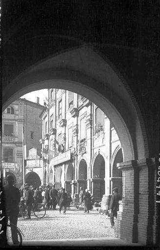 Passants sur la place, vue prise d'un portique