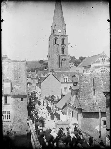 Vue générale de la ville : clocher de l'église, procession dans une rue