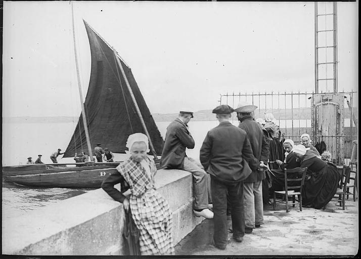 Bretons en costume traditionnel sur la jetée, voilier en mer