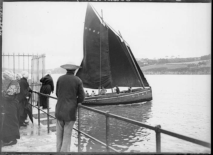 Bretons en costume traditionnel sur la jetée, voilier en mer