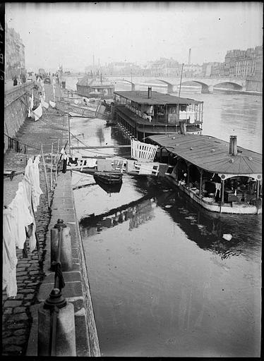 Sur le quai : péniches amarrées, linge étendu, pont à l'arrière-plan