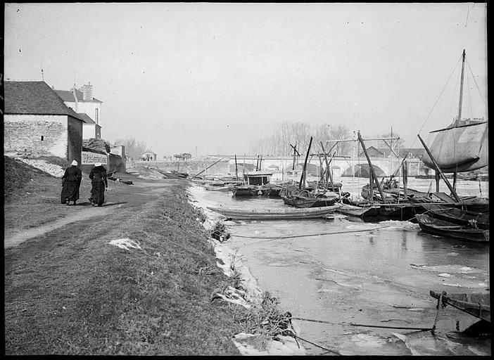 Sur la berge : péniche, barques, pont à l'arrière-plan