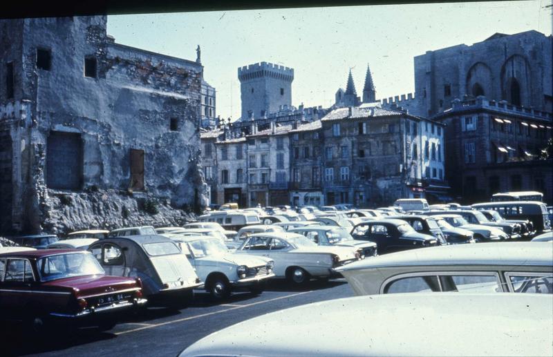 Place du palais : parc de stationnement et îlot de vieux immeubles accolés au Palais des Papes