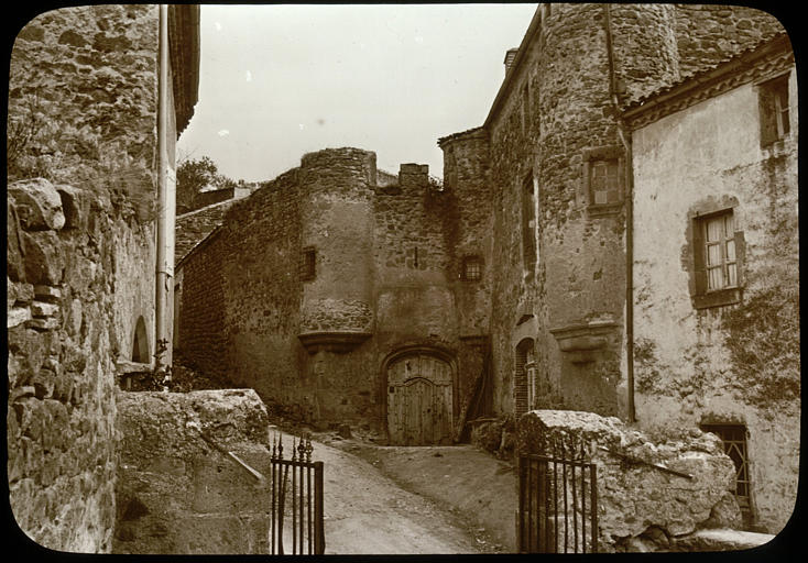 Rue à Montaigut-le-Blanc : chemin avec une grille ouverte et des bâtiments fortifiés à l'arrière-plan