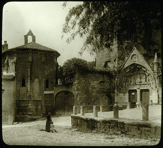 Chapelle de Saint-Emilion : vue d'ensemble prise de la place devant le chevet de la chapelle, à droite le portail de l'église monolithe, une femme et un enfant