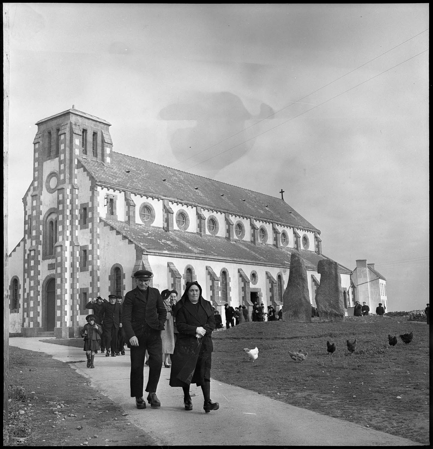 Sortie d’office à l’église paroissiale : fidèles, menhirs et poules