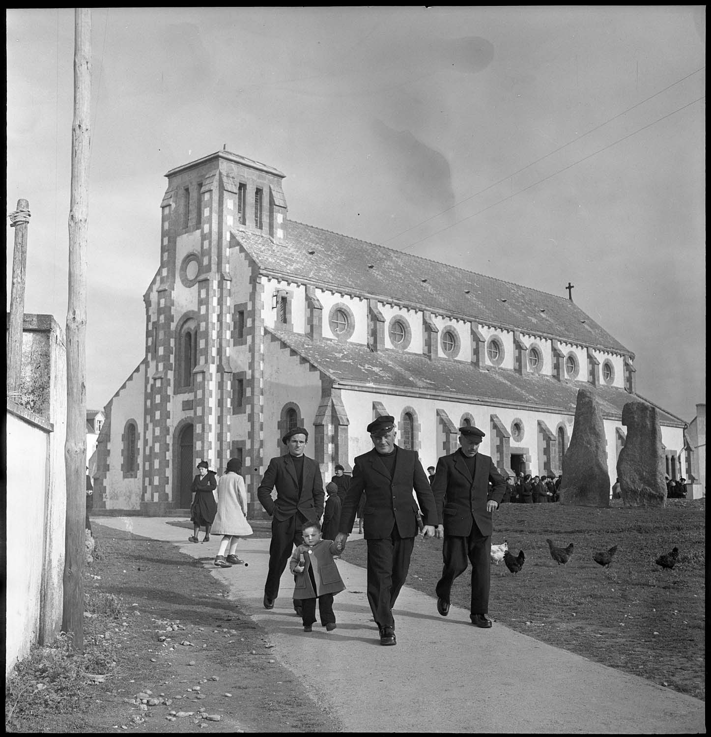 Sortie d’office à l’église paroissiale : fidèles, menhirs et poules