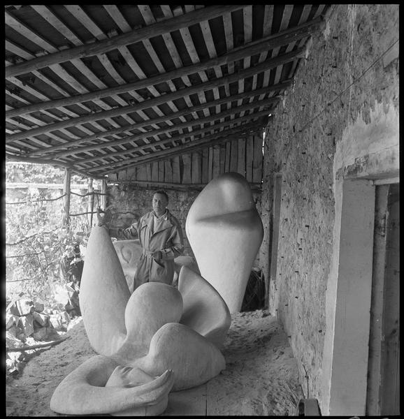 [Portrait de Henri-Georges Adam dans la cour de son atelier au milieu de ses oeuvres, avec 'La femme endormie' au premier plan]