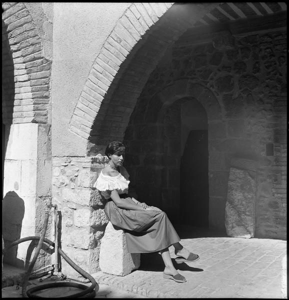 [Jeune femme assise sous une arcade du patio]