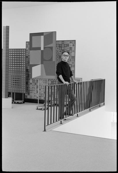 [Portrait de Victor Vasarely appuyé sur la rampe d'escalier de son atelier, à côté de ses oeuvres]