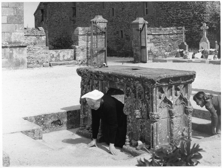 Grand Pardon de Saint-Yves : femme en costume traditionnel passant sous le tombeau du saint, dans le cimetière - © Donation Jack Boulas, Ministère de la Culture (France), Médiathèque du patrimoine et de la photographie, diffusion GrandPalaisRmn Photo