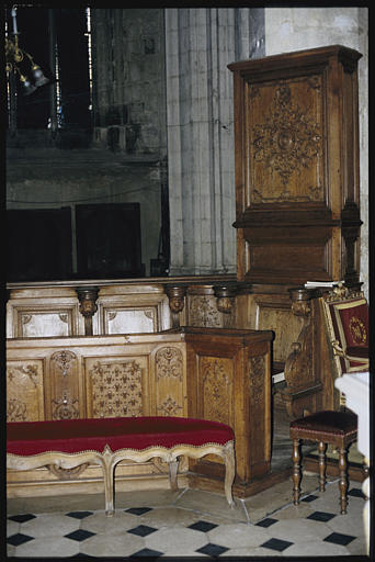 Choeur ; stalles, banquette : bois sculpté de motifs d'arabesques et de fleurs de lys (détail)