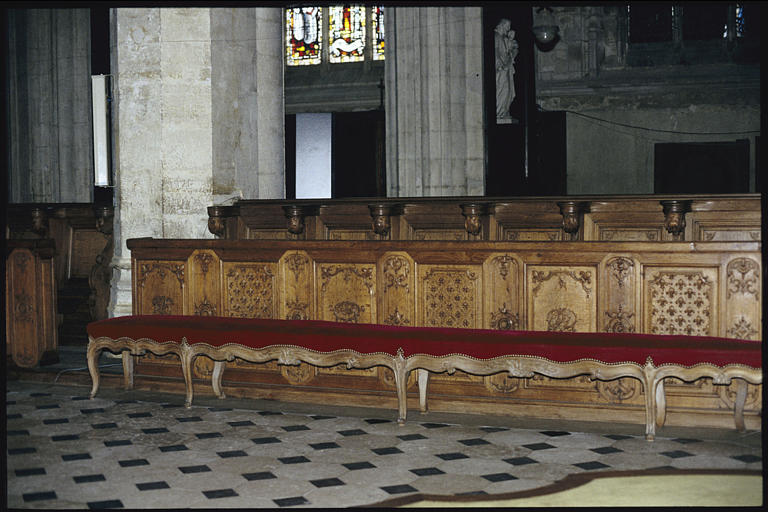 Choeur ; stalles, banquette : bois sculpté de motifs d'arabesques et de fleurs de lys (détail)