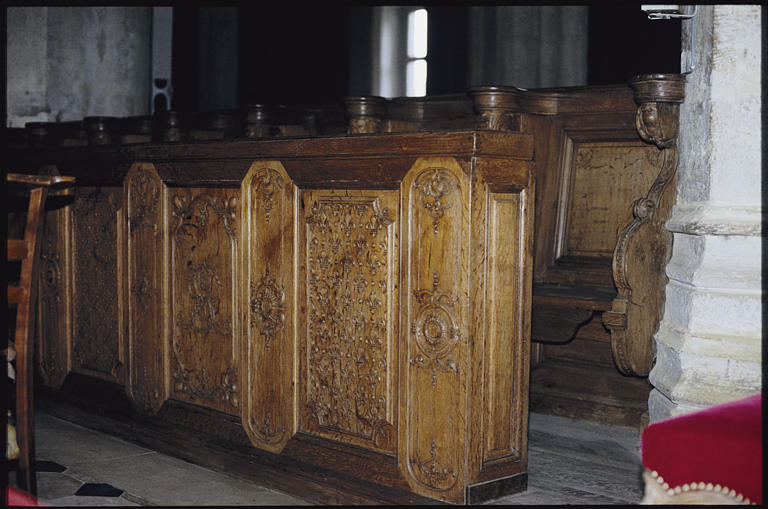 Choeur ; stalles, banquette : bois sculpté de motifs d'arabesques et de fleurs de lys (détail)