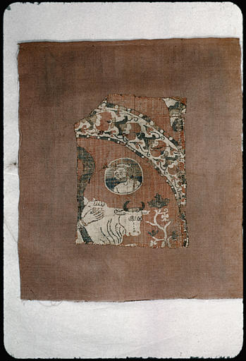 Tissu : fragment, ocre rouge à motifs blancs, représentant un boeuf et un médaillon circulaire avec un visage d'homme