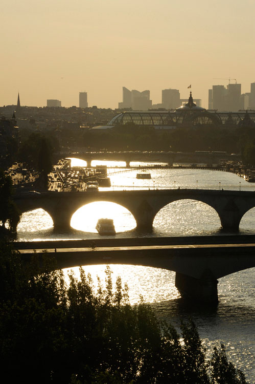 Enfilade de ponts au crépuscule depuis le quai de Conti. À l'arrière-plan, le Grand Palais et la Défense