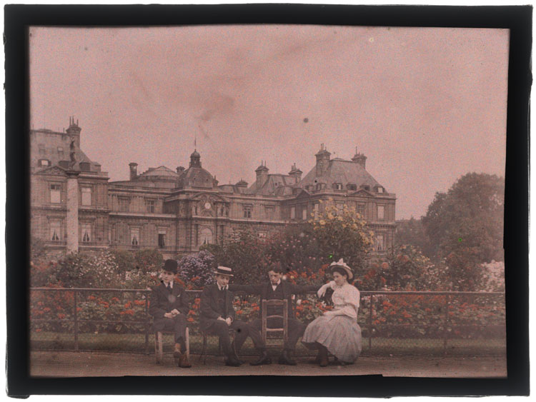 Marthe et Jean Antoine en compagnie de deux jeunes hommes assis devant un parterre de fleurs, le palais du Luxembourg en arrière-plan