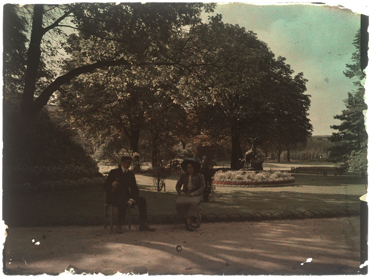 Marthe et Jean Antoine dans un jardin : Marthe portant un chapeau bleu et Jean une casquette, La harde des cerfs d'Arthur Jacques Le Duc en arrière-plan