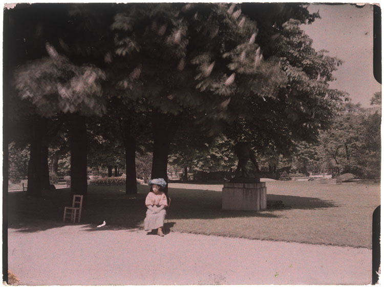 Marthe Antoine assise dans une allée du jardin, Les Lutteurs d'Auguste Ottin en arrière-plan