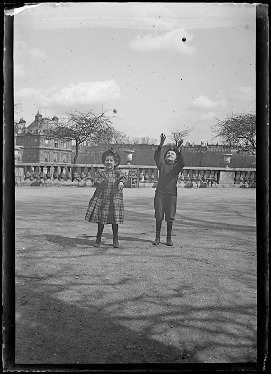 Marthe et Jean Antoine jouant à la balle côte à côte face au photographe, le palais en arrière-plan